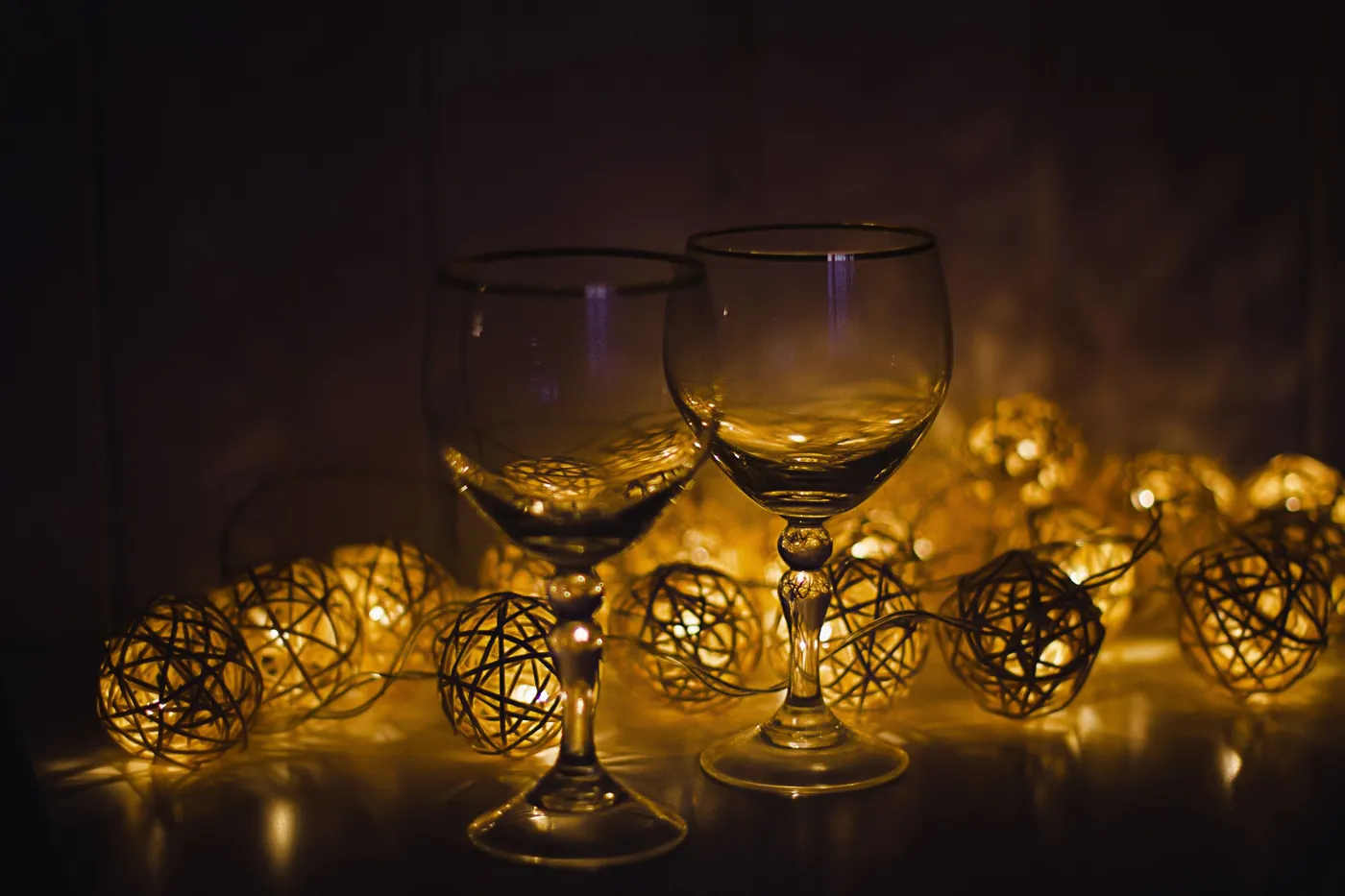 Two wine glasses beside warm string lights