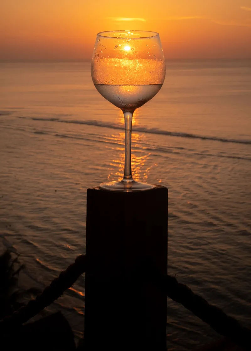 A glass of white wine against a sunset over the sea